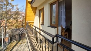 A balcony with a black railing, a wooden floor, and a view of a tree and buildings in the background. - VISITzakopane City Apartments (Zakopane)