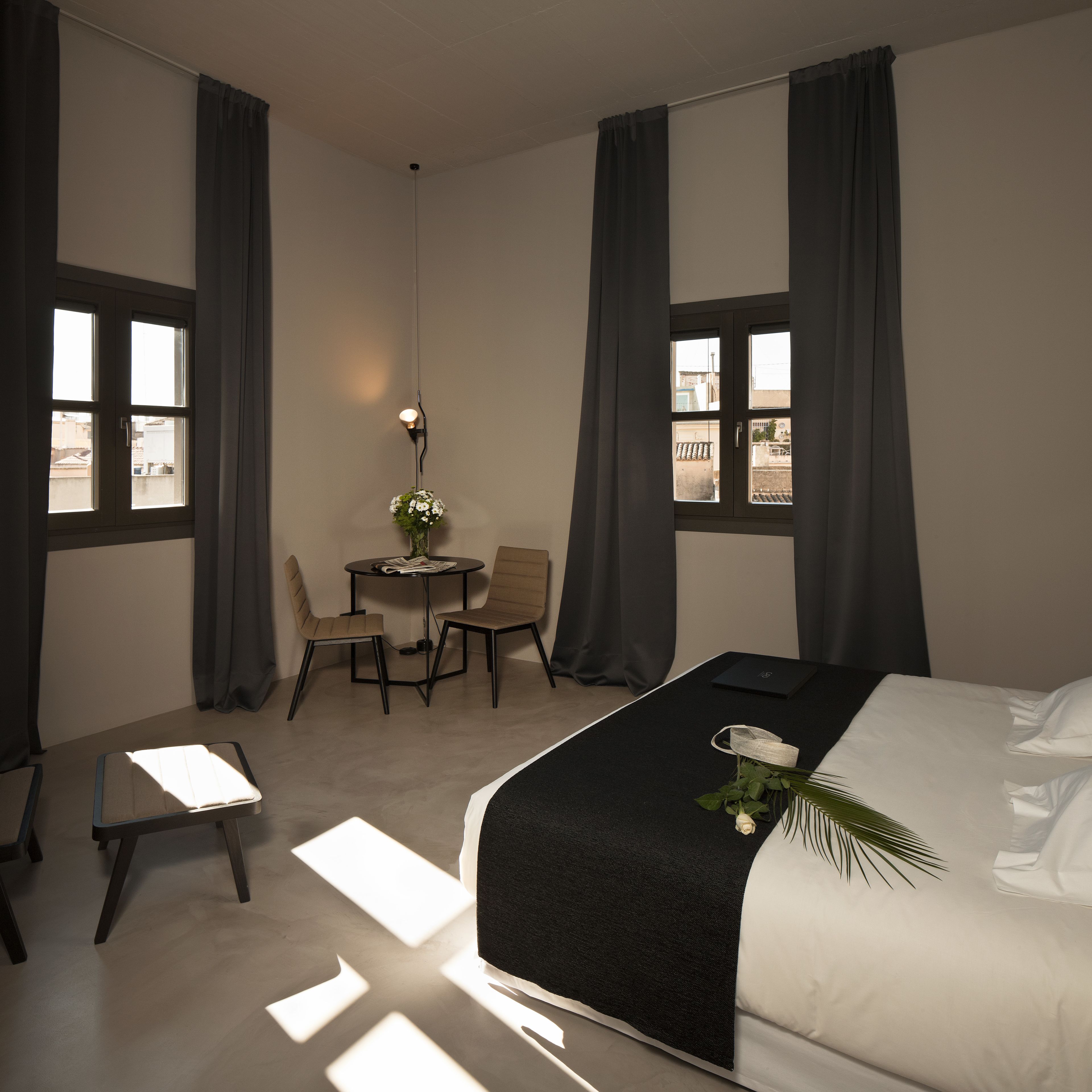 A hotel room with a bed, a desk with two chairs, a small table with a lamp, and a window with curtains.