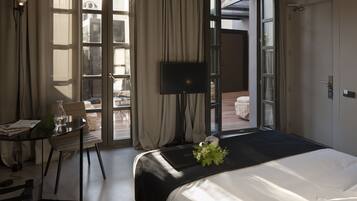 Habitación de hotel con cama, escritorio, silla, televisor y vistas al exterior.