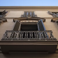 Fachada de edificio con balcones de intrincada rejería, un elemento decorativo central y un diseño simétrico.