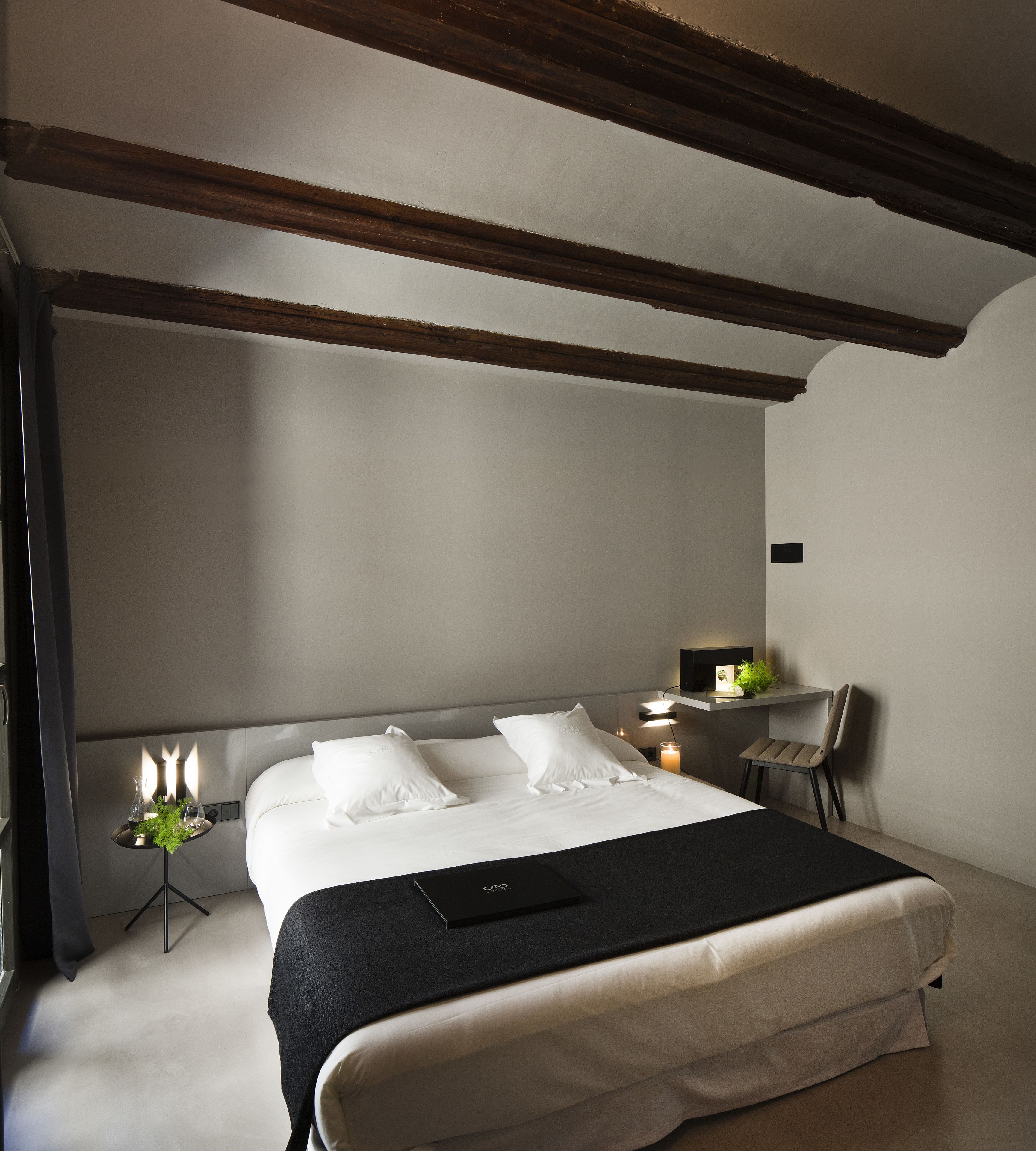 A bedroom with a large bed, a bedside table with a lamp, a chair, and a desk with a computer.