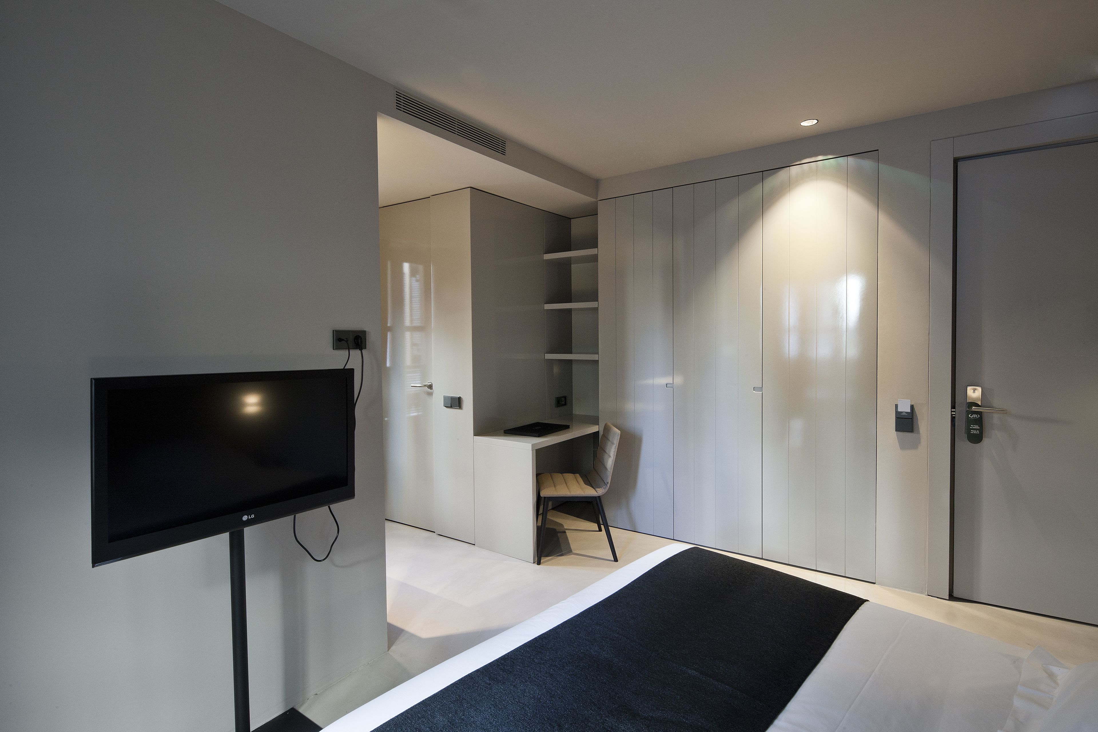 A modern hotel room with a flat-screen TV, a desk, a chair, and built-in wardrobes.