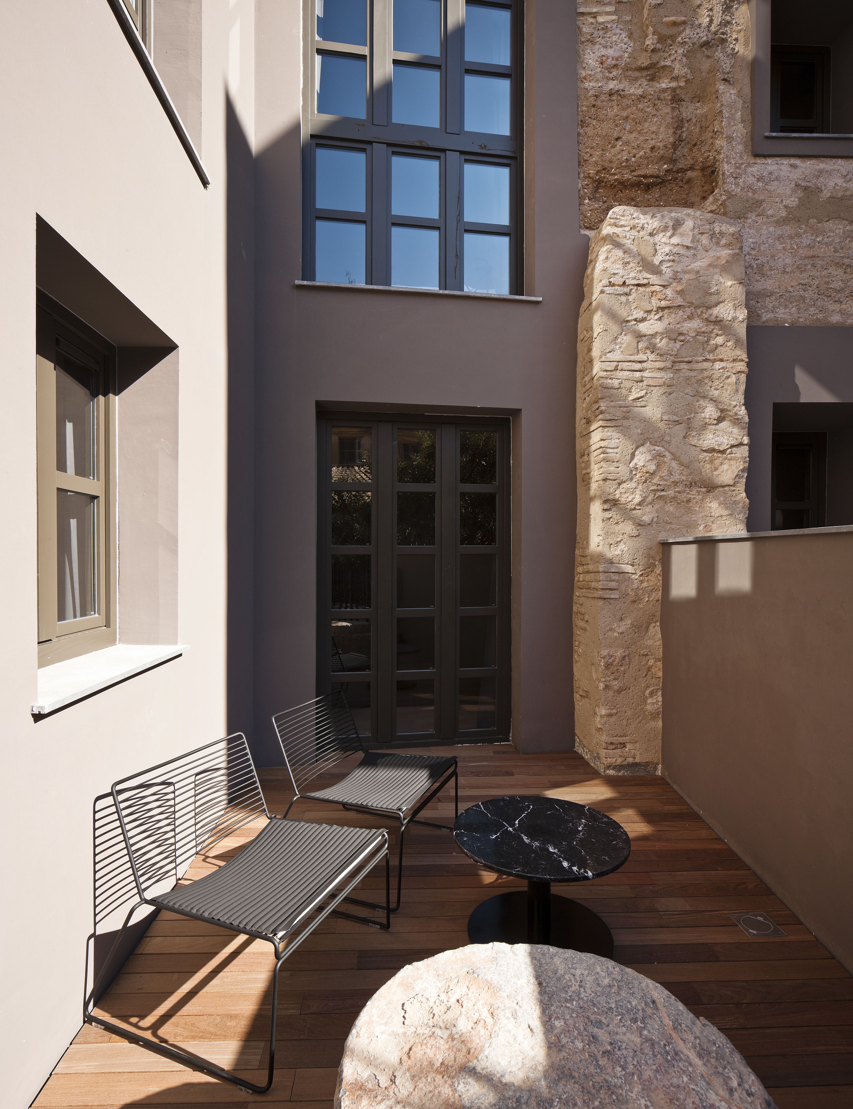 A modern outdoor patio with two metal chairs, a round table, and a stone accent piece.