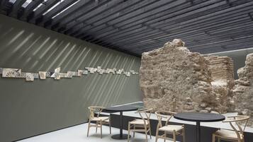 Un espai interior amb un disseny modern, que presenta una sèrie d'obres d'art a la paret, una gran escultura de roca i una zona de seients amb taules i cadires.