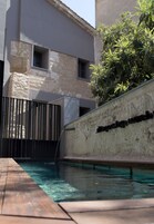 Una piscina con cubierta de madera, un muro de piedra con una placa con un nombre, y un edificio de diseño moderno.