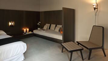 Een moderne hotelkamer met een bed, een slaapbank, een klein tafeltje, een stoel en wandlampen.