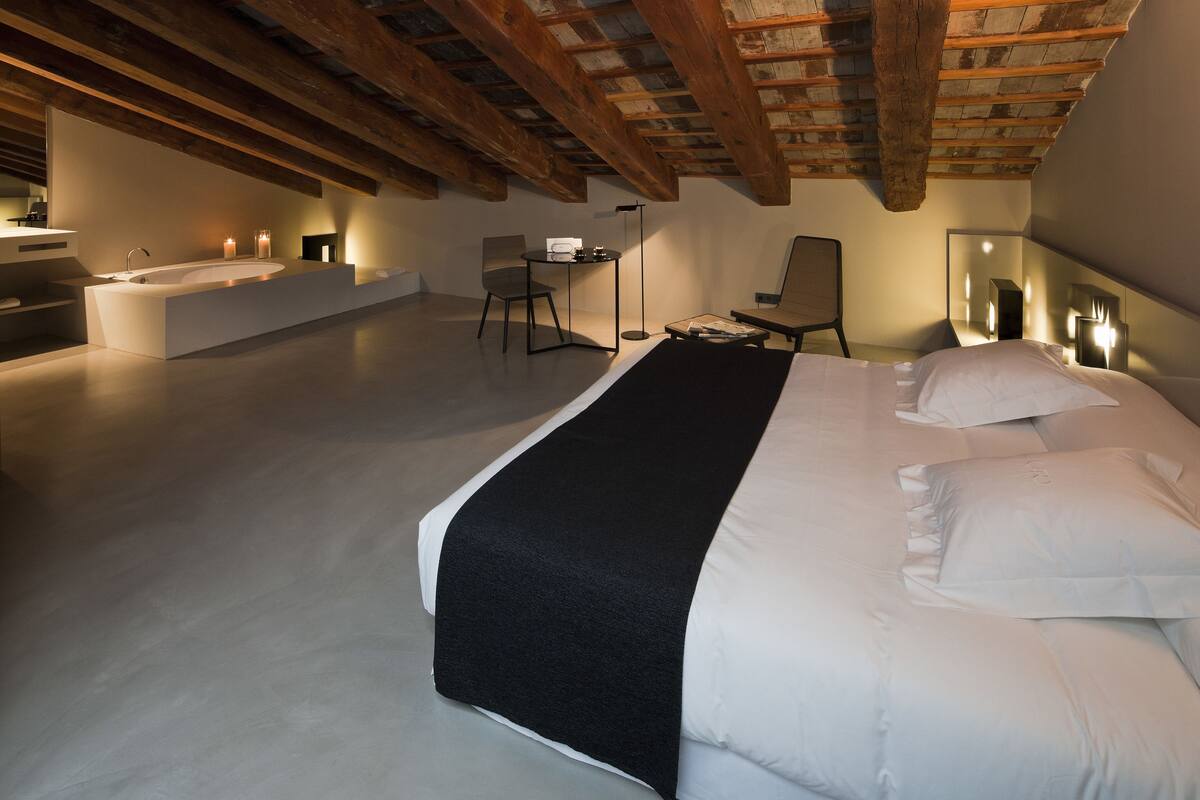 Un dormitorio moderno con una cama grande, un escritorio pequeño, una silla, una mesita de noche y un baño con bañera.