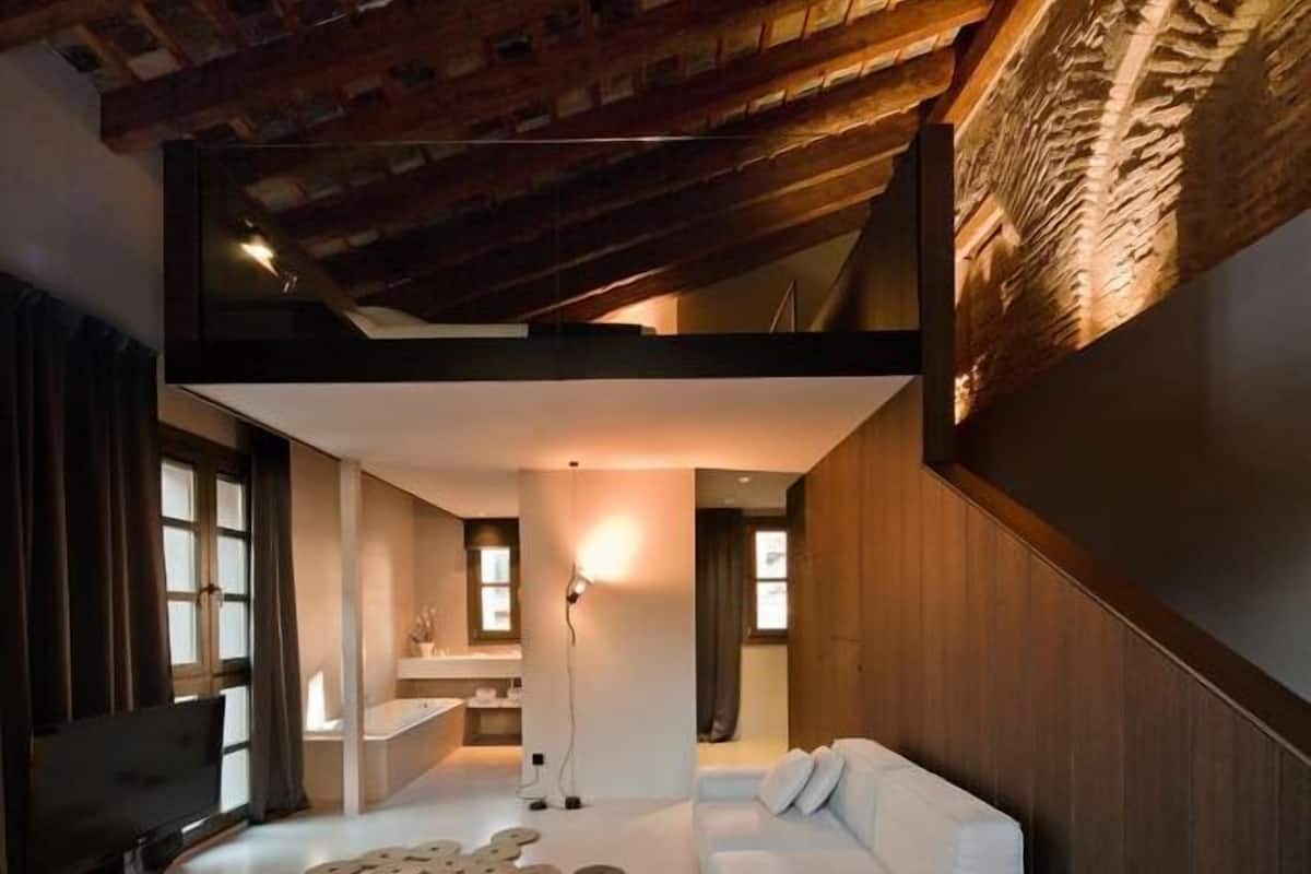Una sala de estar moderna con un sofá blanco, un televisor de pantalla plana y un techo con vigas de madera a la vista.