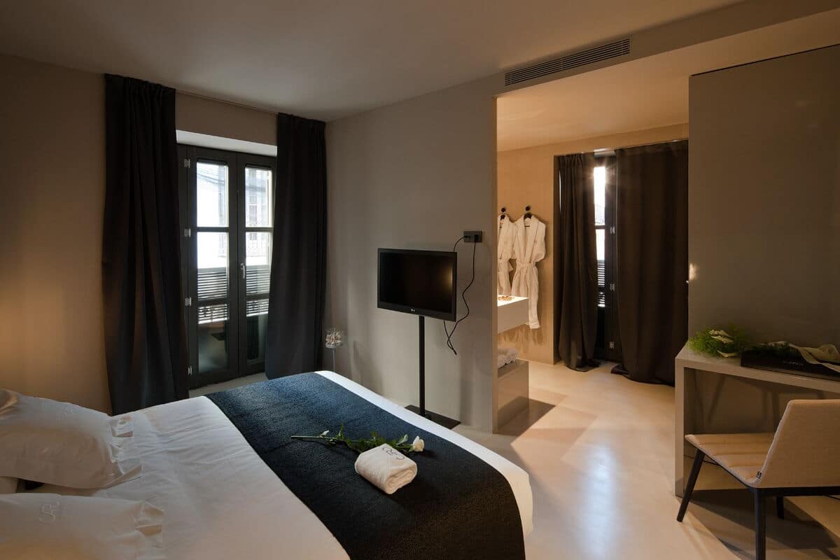 Habitación de hotel con cama, televisor, escritorio y baño visible a través de una puerta abierta.