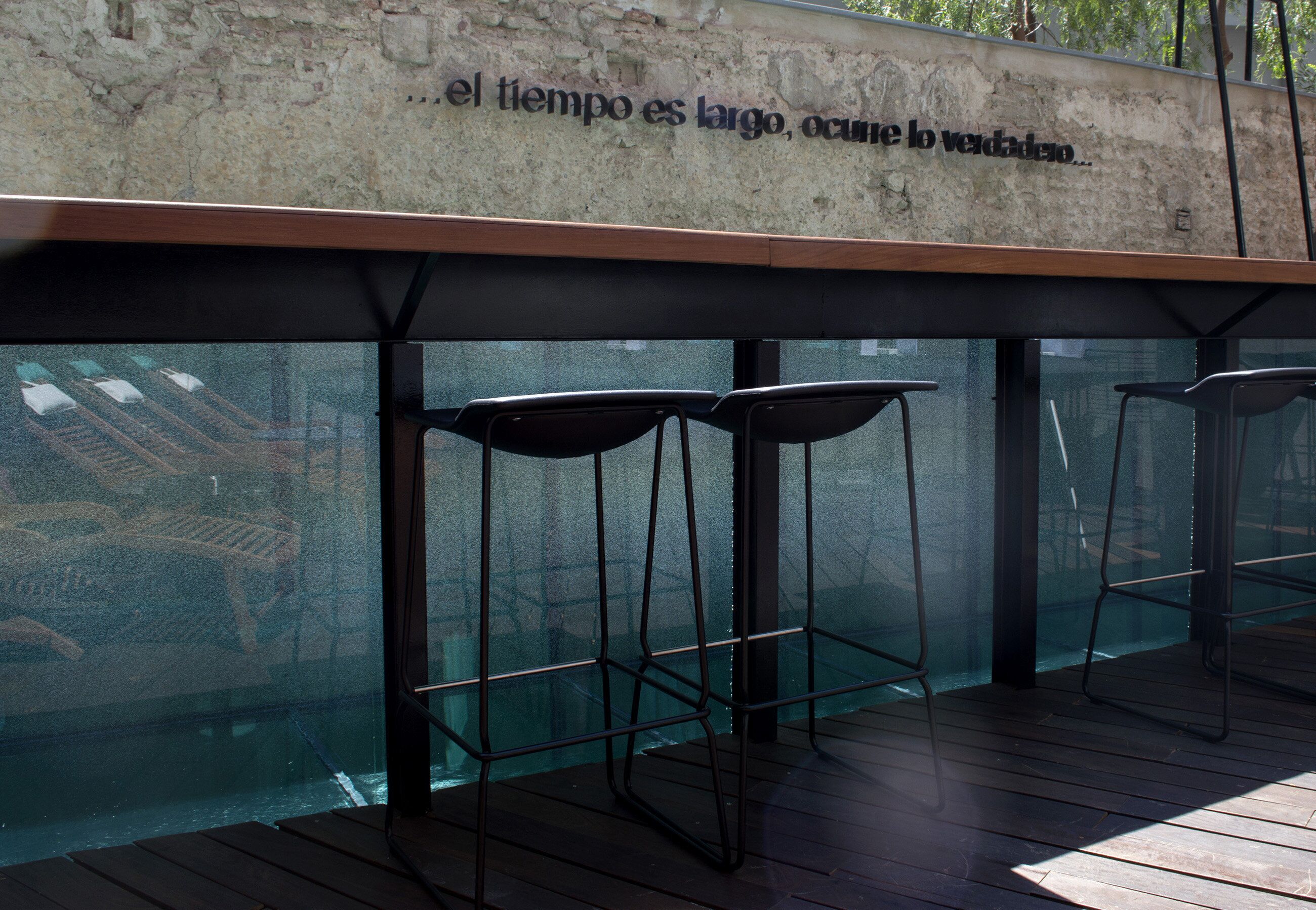A bar area with high stools and a concrete wall with text.