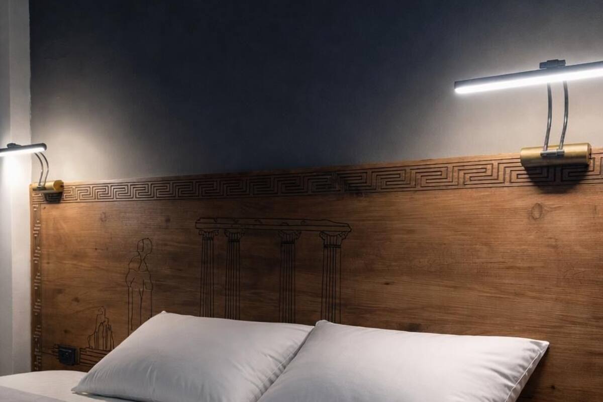 Un lit avec une literie blanche, une tête de lit en bois ornée d’un motif géométrique et une table de chevet avec une lampe.