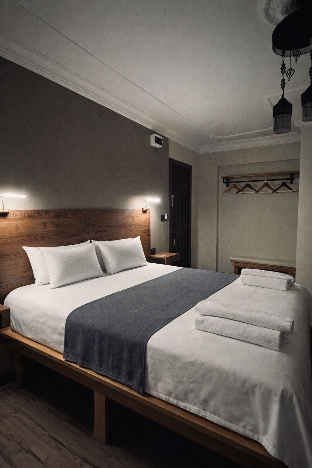 A neatly made bed with a wooden headboard, bedside tables, and a hanging light fixture.