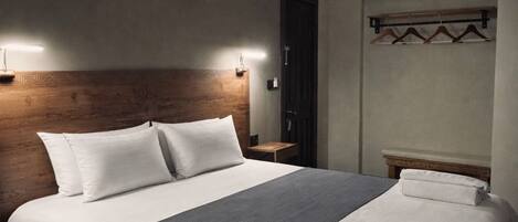 A neatly made bed with a wooden headboard, bedside tables, and a hanging light fixture.