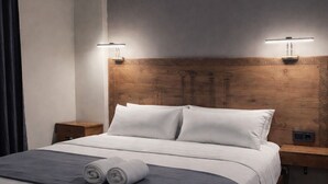 Un lit bien fait, avec du linge de lit blanc, deux lampes de chevet et une tête de lit en bois ornée d’un motif décoratif.