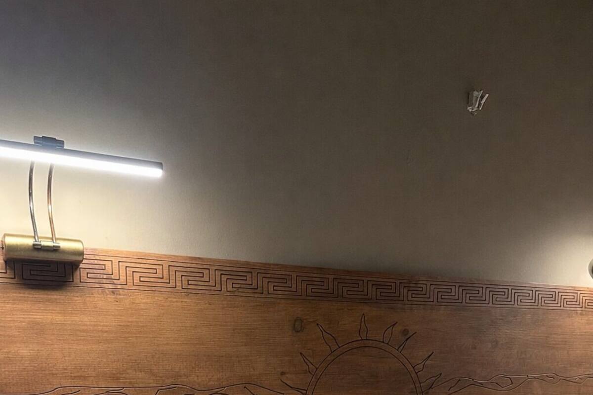 Un lit bien fait, avec du linge de lit blanc, une tête de lit en bois ornée d’un motif solaire et une table de chevet avec une lampe.