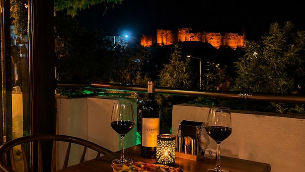 Une table dressée pour deux personnes, avec des verres à vin, une bouteille et une bougie, donnant sur un château illuminé la nuit.