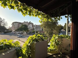 Vista de una calle con coches aparcados, un muro de piedra y un edificio con una bandera.