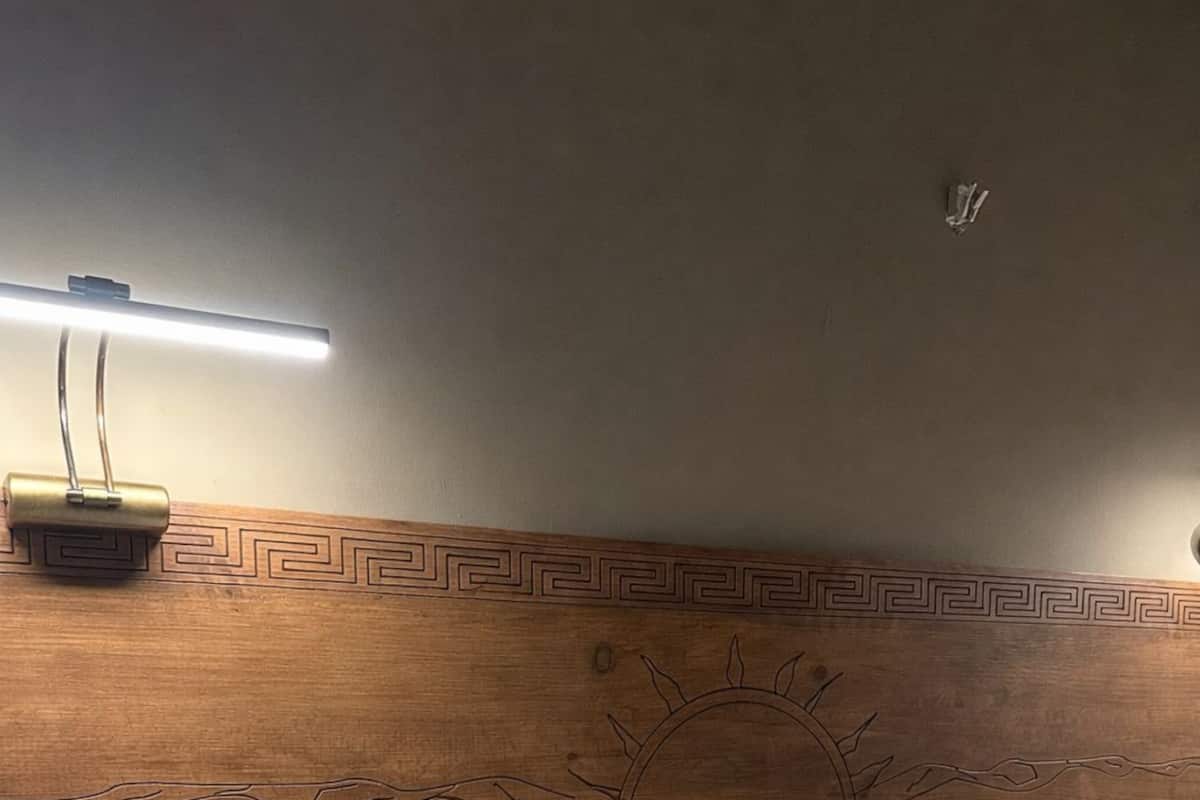 Un lit bien fait, avec du linge de lit blanc, une tête de lit en bois ornée d’un motif solaire et une table de chevet avec une lampe.
