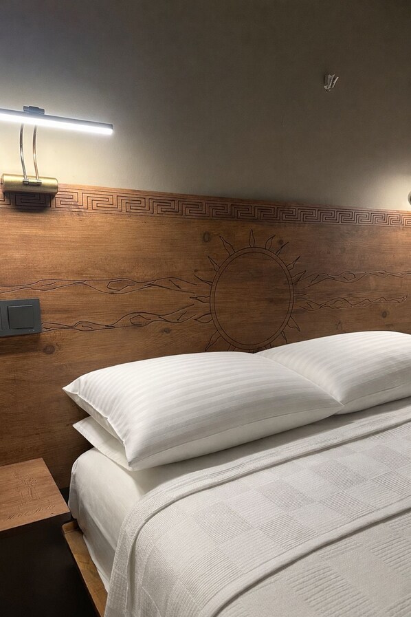 Un lit bien fait, avec du linge de lit blanc, une tête de lit en bois ornée d’un motif solaire et une table de chevet avec une lampe.