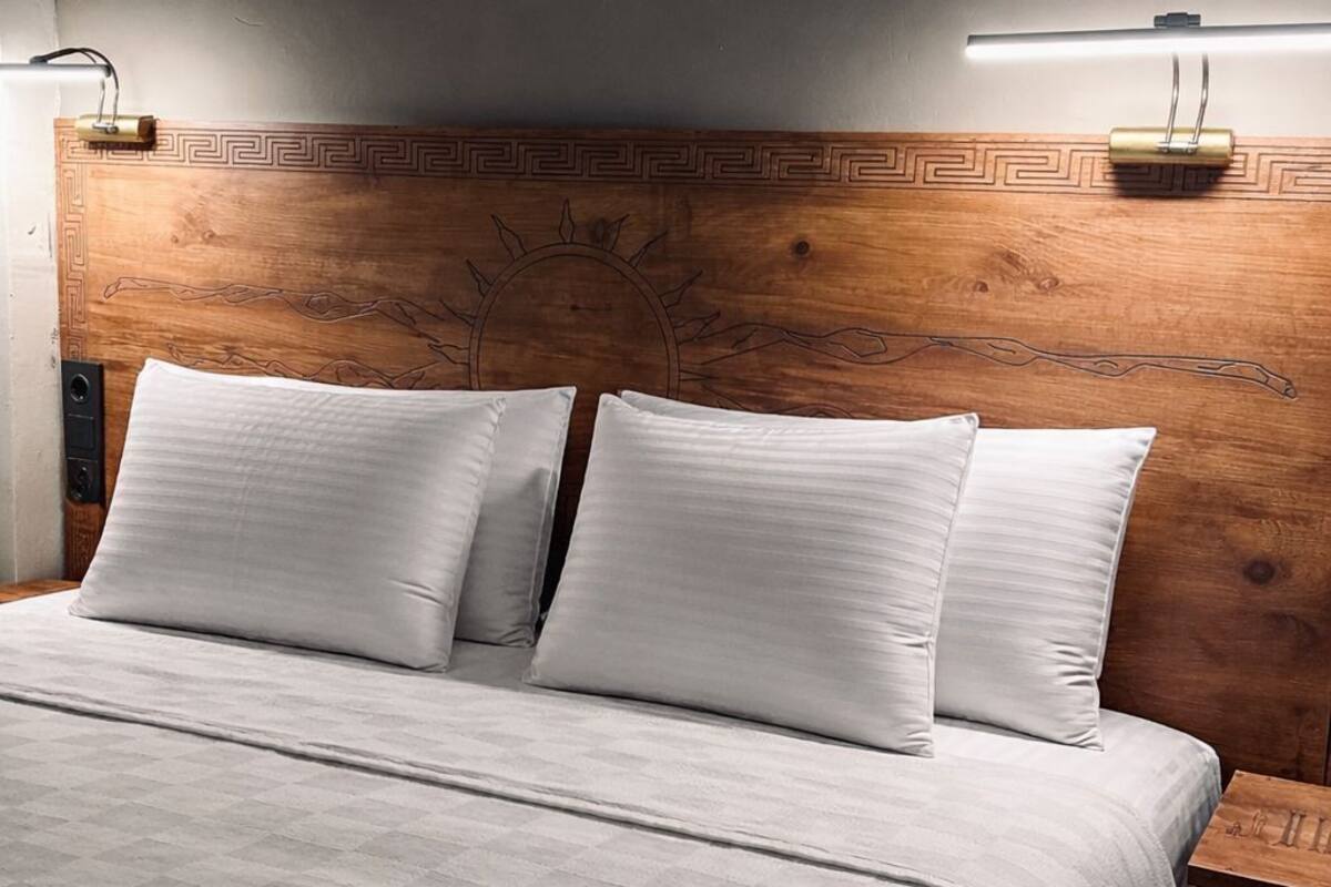 Un lit avec une tête de lit en bois, deux tables de chevet et un luminaire fixé au mur.