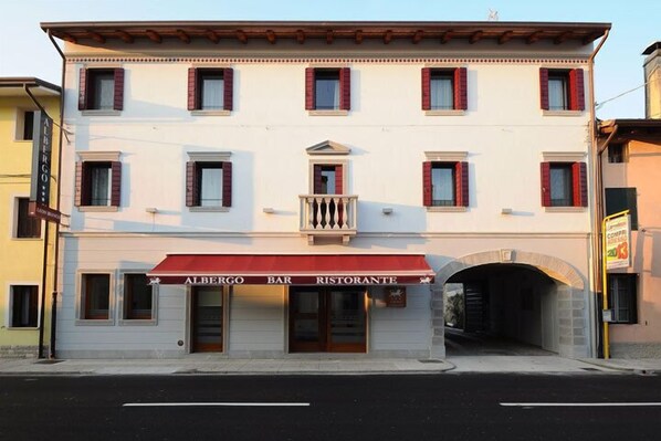 A two-story building with a red awning labeled "ALBERGO BAR RISTORANTE." - Albergo Leon Bianco (Gonars)
