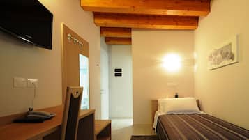 A hotel room with a wooden ceiling, a bed with a striped bedspread, a desk with a telephone, and a television mounted on the wall.