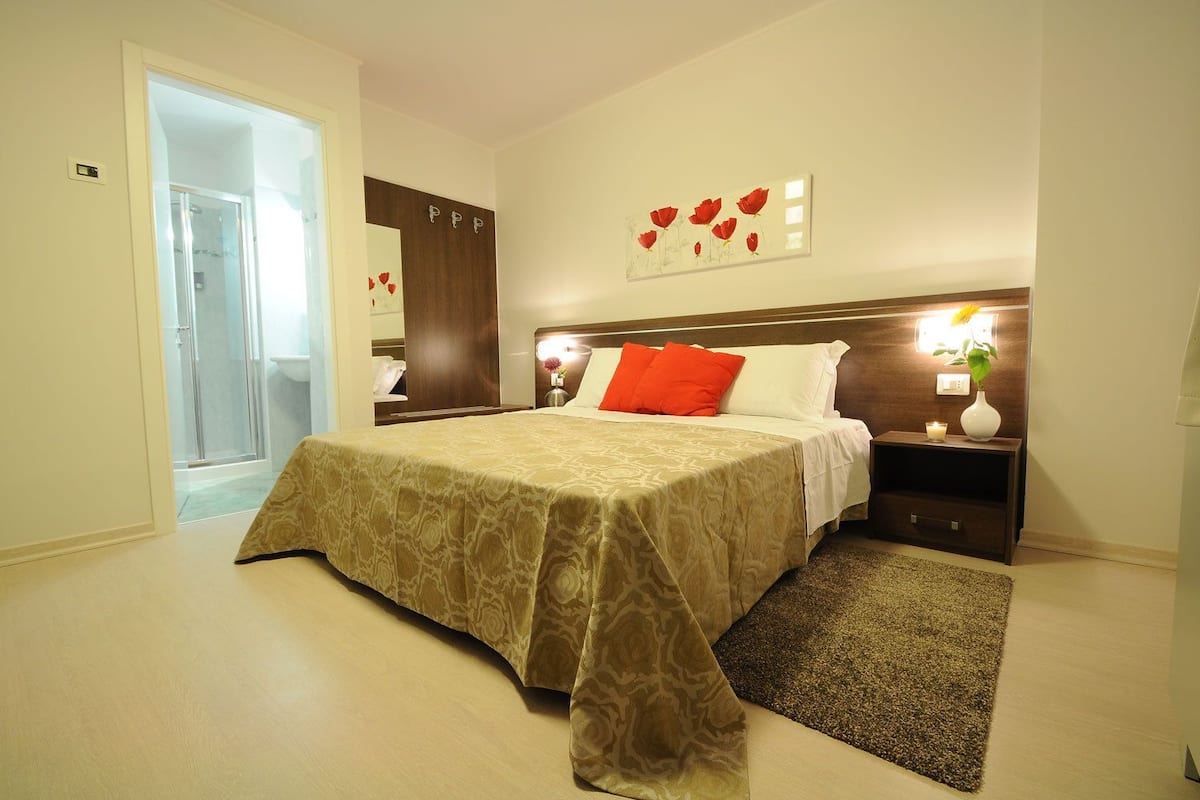 A hotel room with a bed, a nightstand, a mirror, and a door leading to a bathroom.