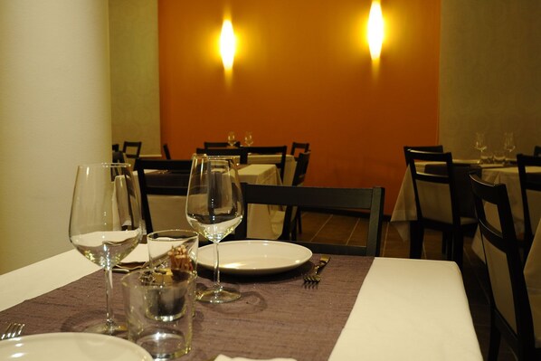 A dining table set with wine glasses, a plate, and cutlery, with chairs around it.