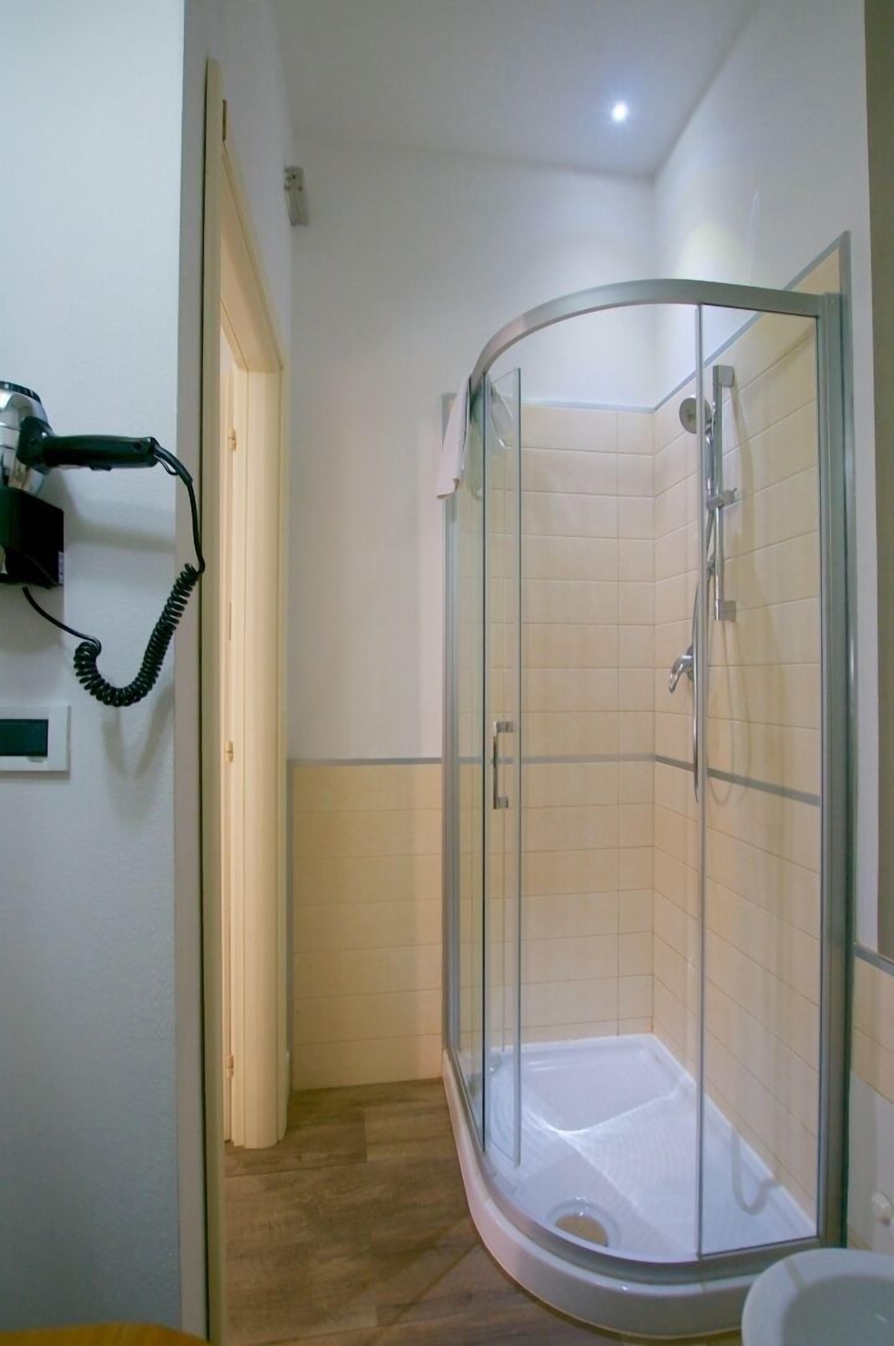 A small, enclosed shower area with a glass door, a toilet, and a hairdryer on a wall.