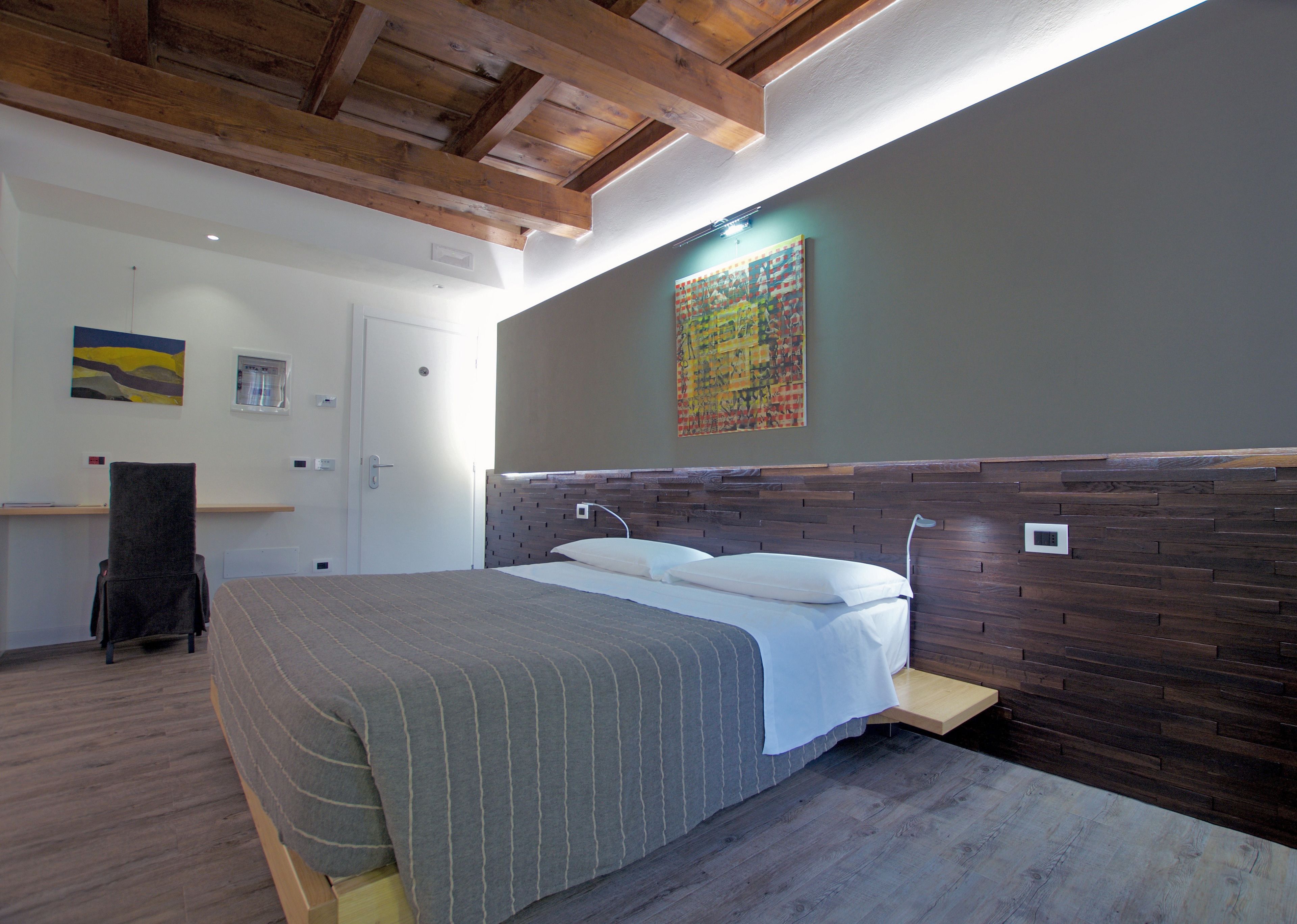 A bedroom with a wooden headboard, a bed with a striped bedspread, a bedside table, a chair, and artwork on the walls.