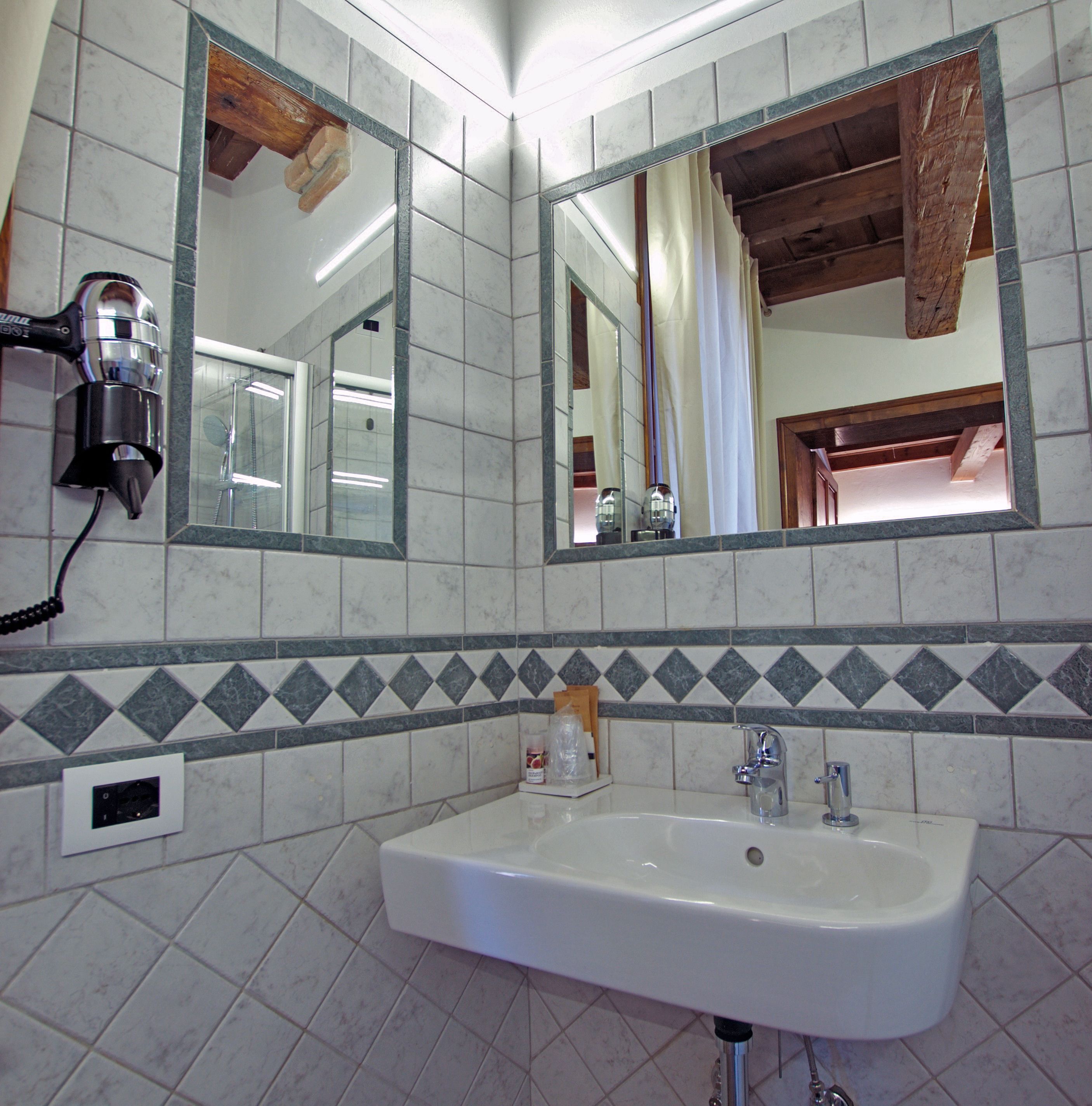 A bathroom with a white sink, two mirrors, and a hairdryer on the wall.
