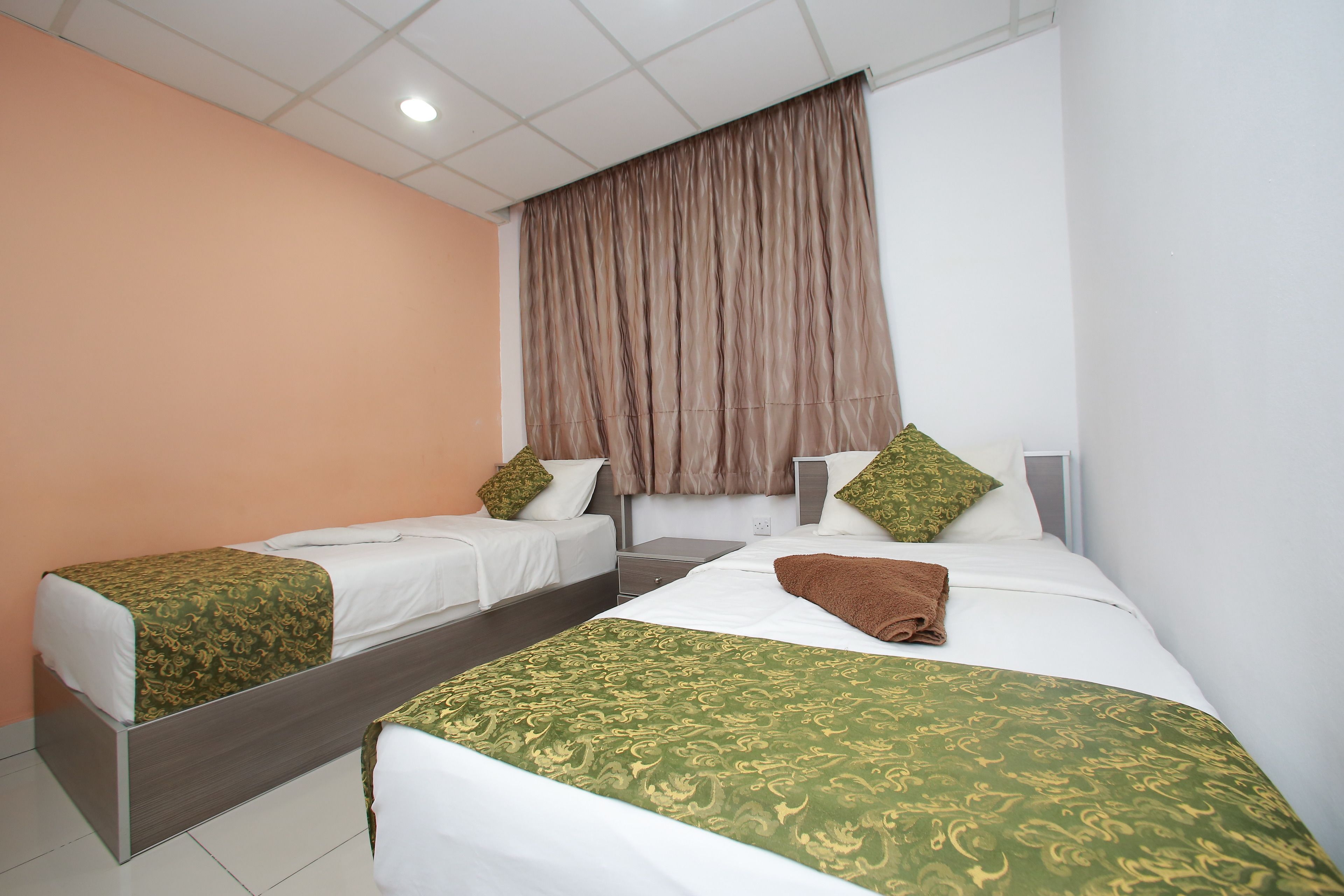Habitación de hotel con dos camas individuales, una cama grande y una mesita de noche.
