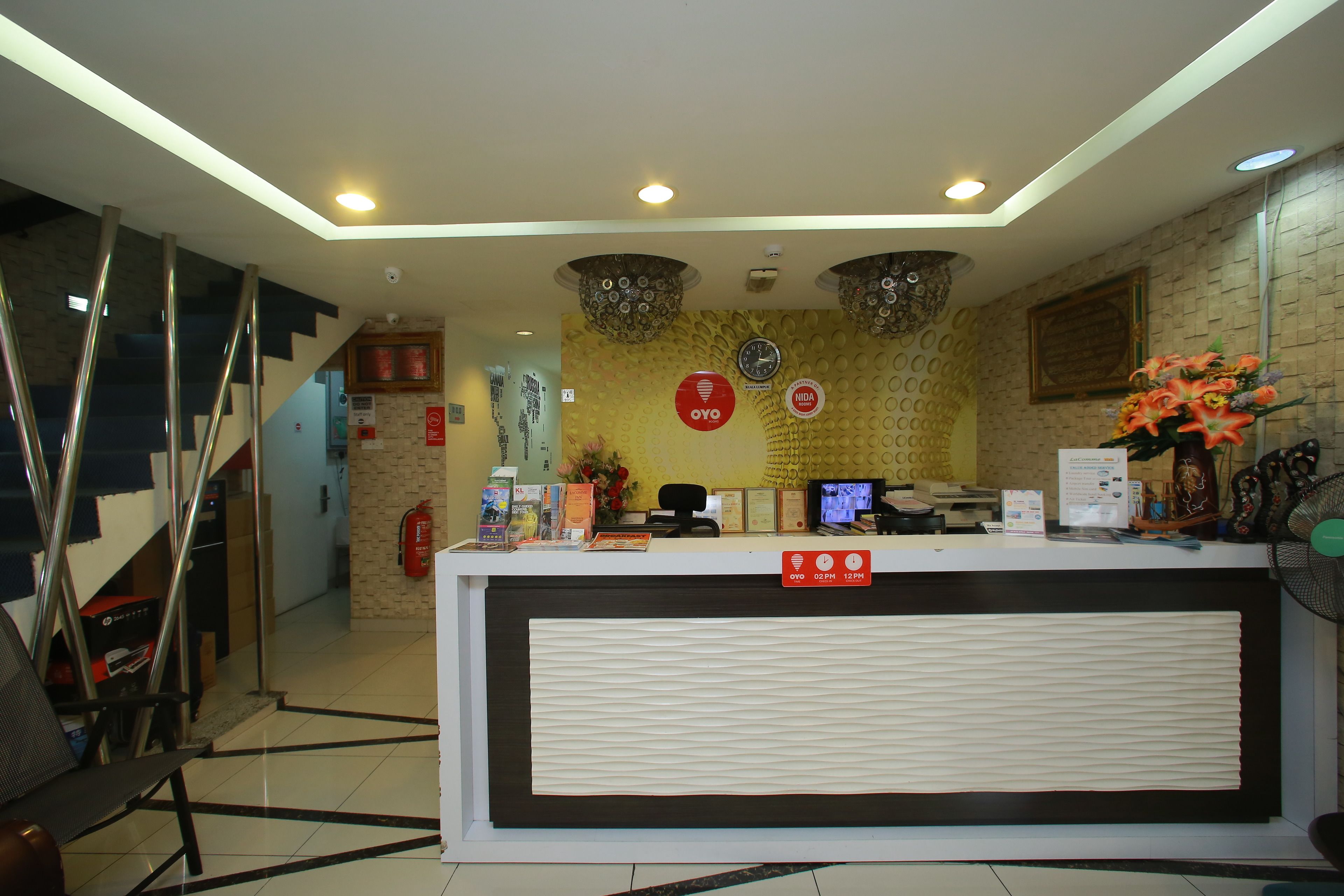 A reception desk with a clock, a fire extinguisher, and a sign indicating the hotel name.