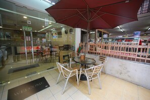 A restaurant with a glass partition, a round table with chairs, and a red umbrella. - LaComme Inn (Kuala Lumpur)