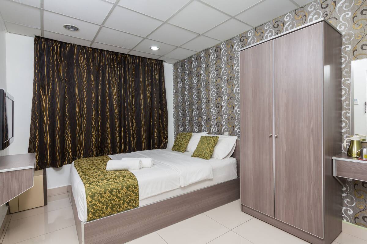 A bedroom with a bed, a wardrobe, a desk, and a television.