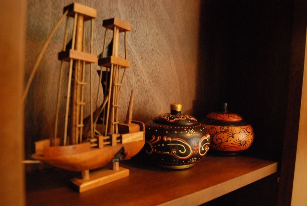 A wooden ship model, a decorative ceramic pot, and a ceramic container on a shelf.