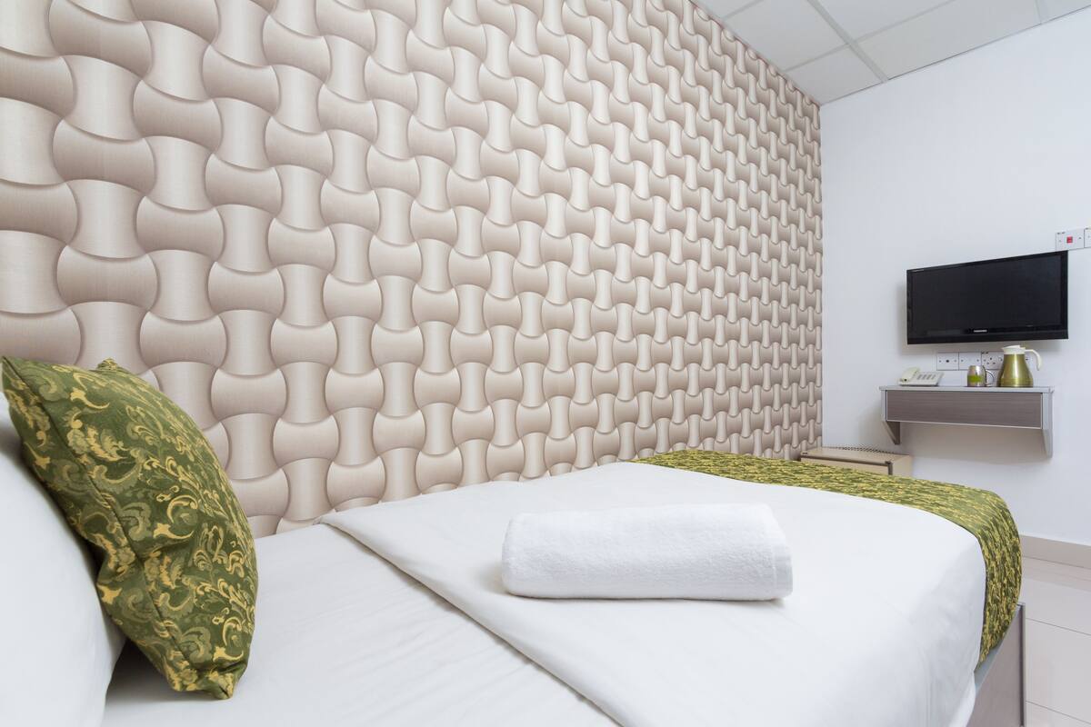 A hotel room with a modern headboard, a flat-screen TV, and a bedside table with a phone and a vase.