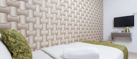 A hotel room with a modern headboard, a flat-screen TV, and a bedside table with a phone and a vase.