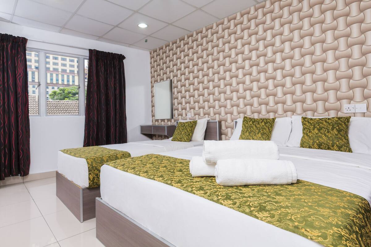 A hotel room with two beds, a patterned wall, a window with curtains, and a mirror.