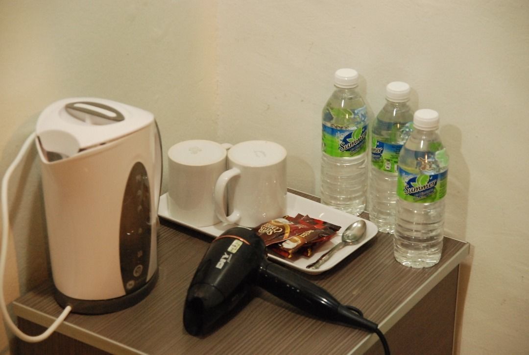 A hotel room with a coffee maker, two mugs, three bottles of water, a hairdryer, and a plate with snacks.