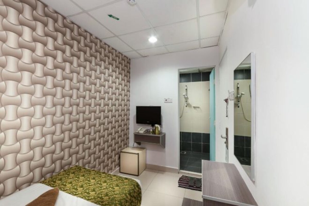 A modern hotel room with a patterned wall, a bed, a TV, a small table, and a shower area.