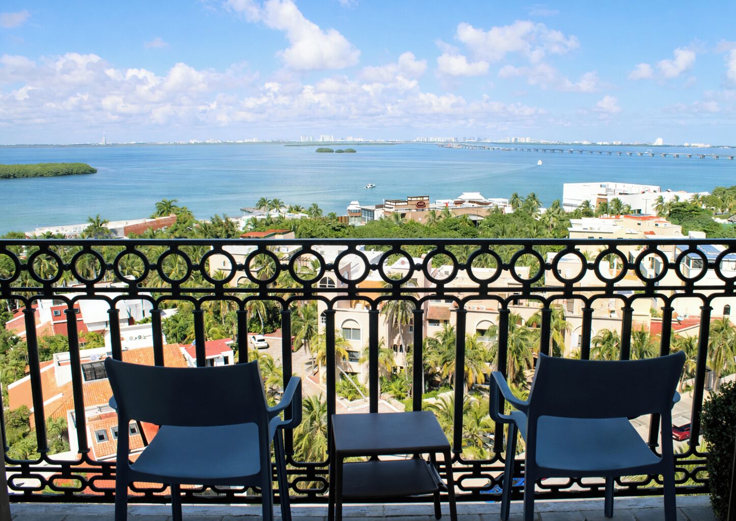 Ein Balkon mit drei Stühlen, der Blick auf die Küste mit Gebäuden und einer Brücke freigibt.