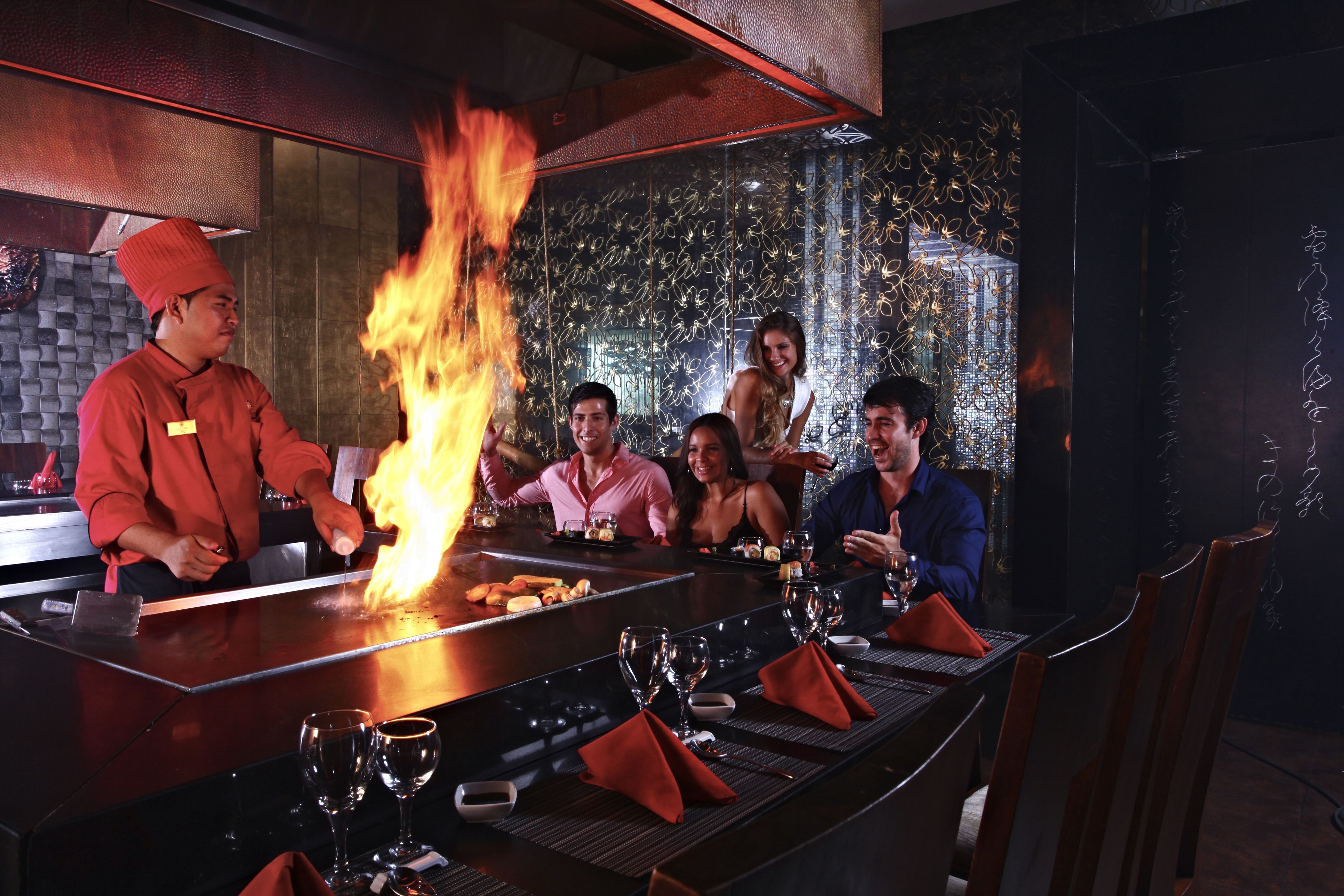 A bar with a grill, seated guests, and a decorative wall.