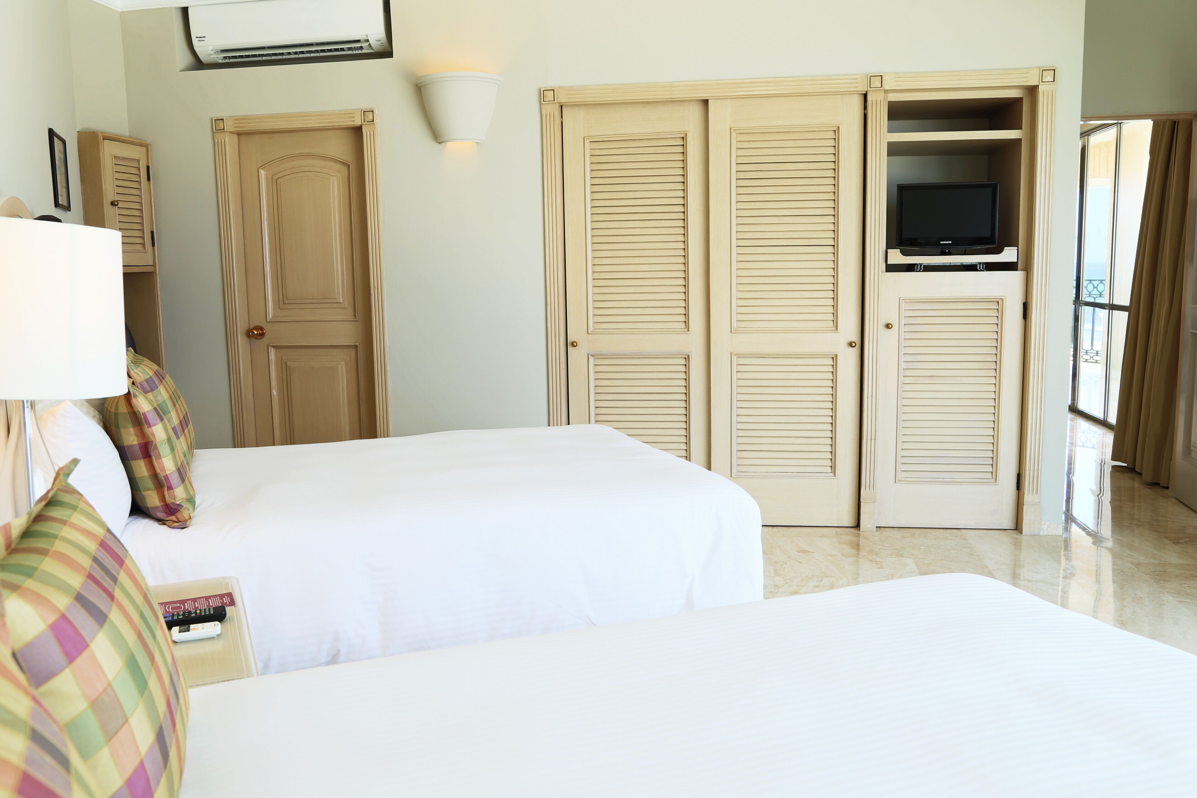 A hotel room with two beds, a television on a shelf, and a wardrobe with sliding doors.