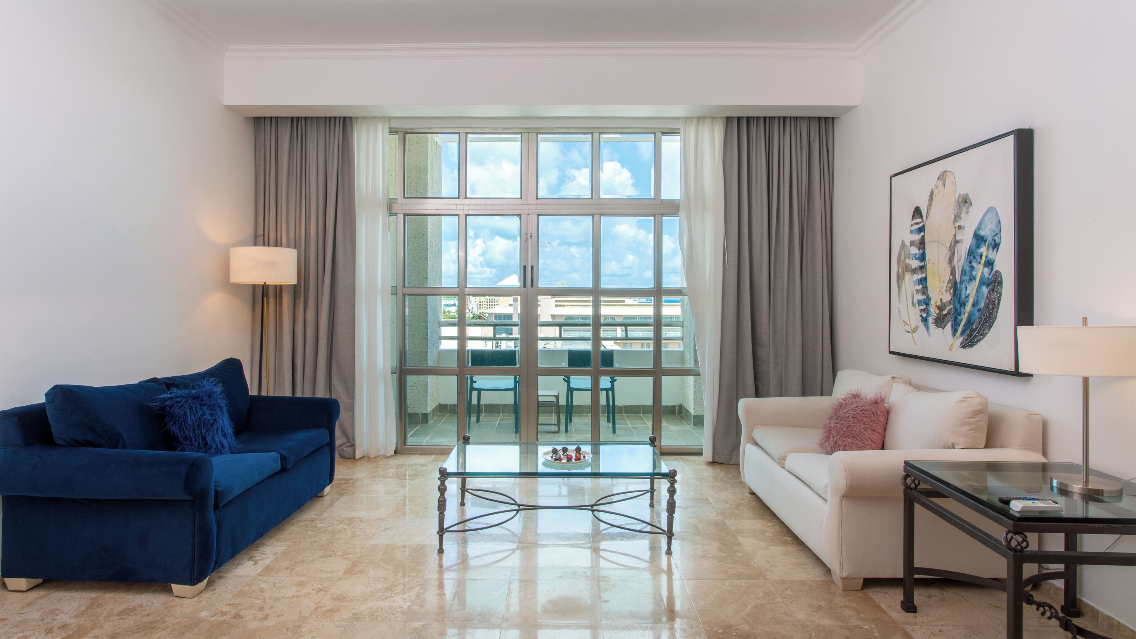 Una sala de estar moderna con un sofá azul, un sofá blanco, una mesa de centro de vidrio y un cuadro en la pared.