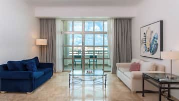 Una sala de estar moderna con un sofá azul, un sofá blanco, una mesa de centro de vidrio y un cuadro en la pared.