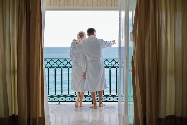 A couple in white robes standing at a balcony with a view of the sea. - Sandos Cancún All Inclusive - Adults Only (Cancun)