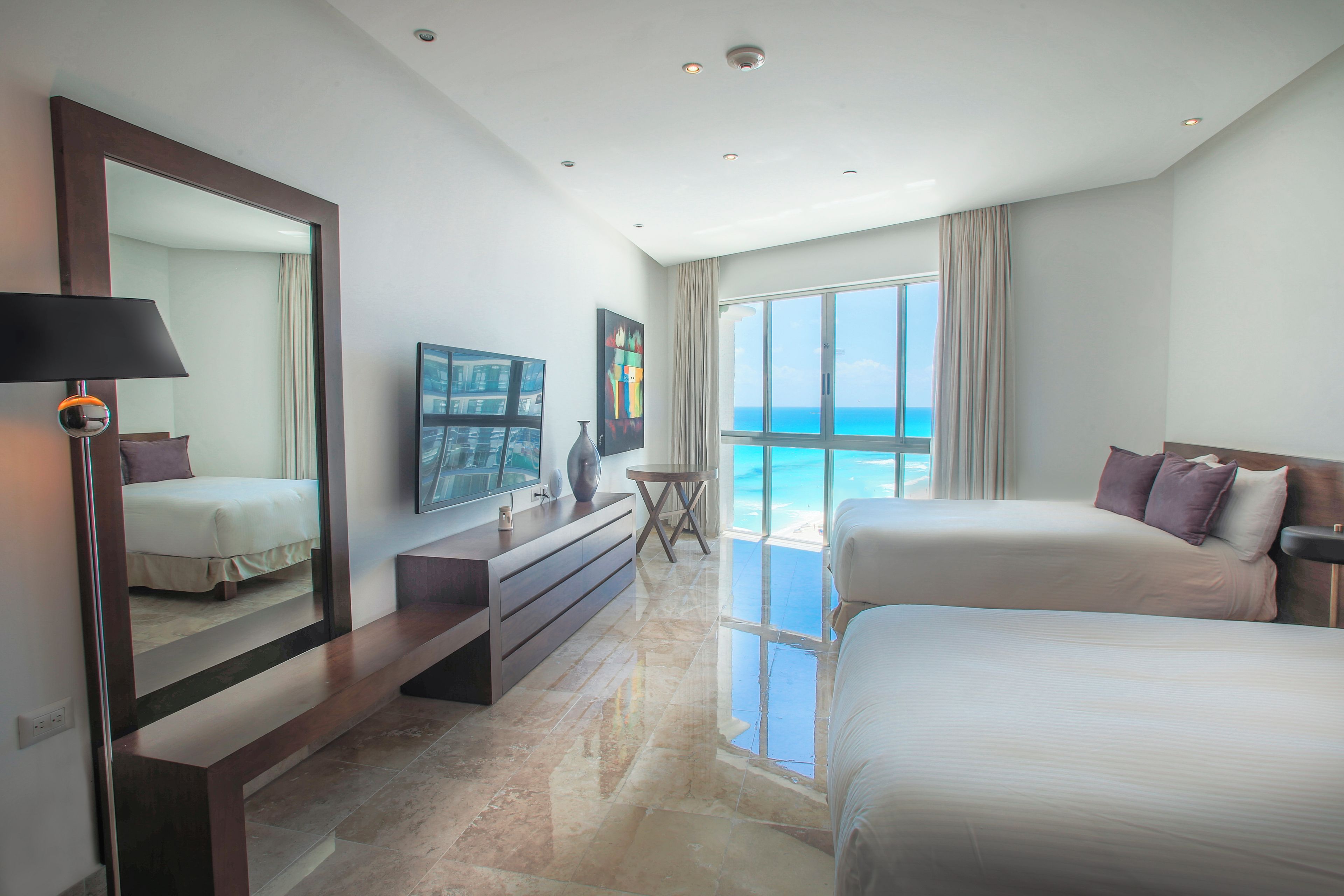 A modern hotel room with a large bed, a TV, a desk, and a view of the ocean.