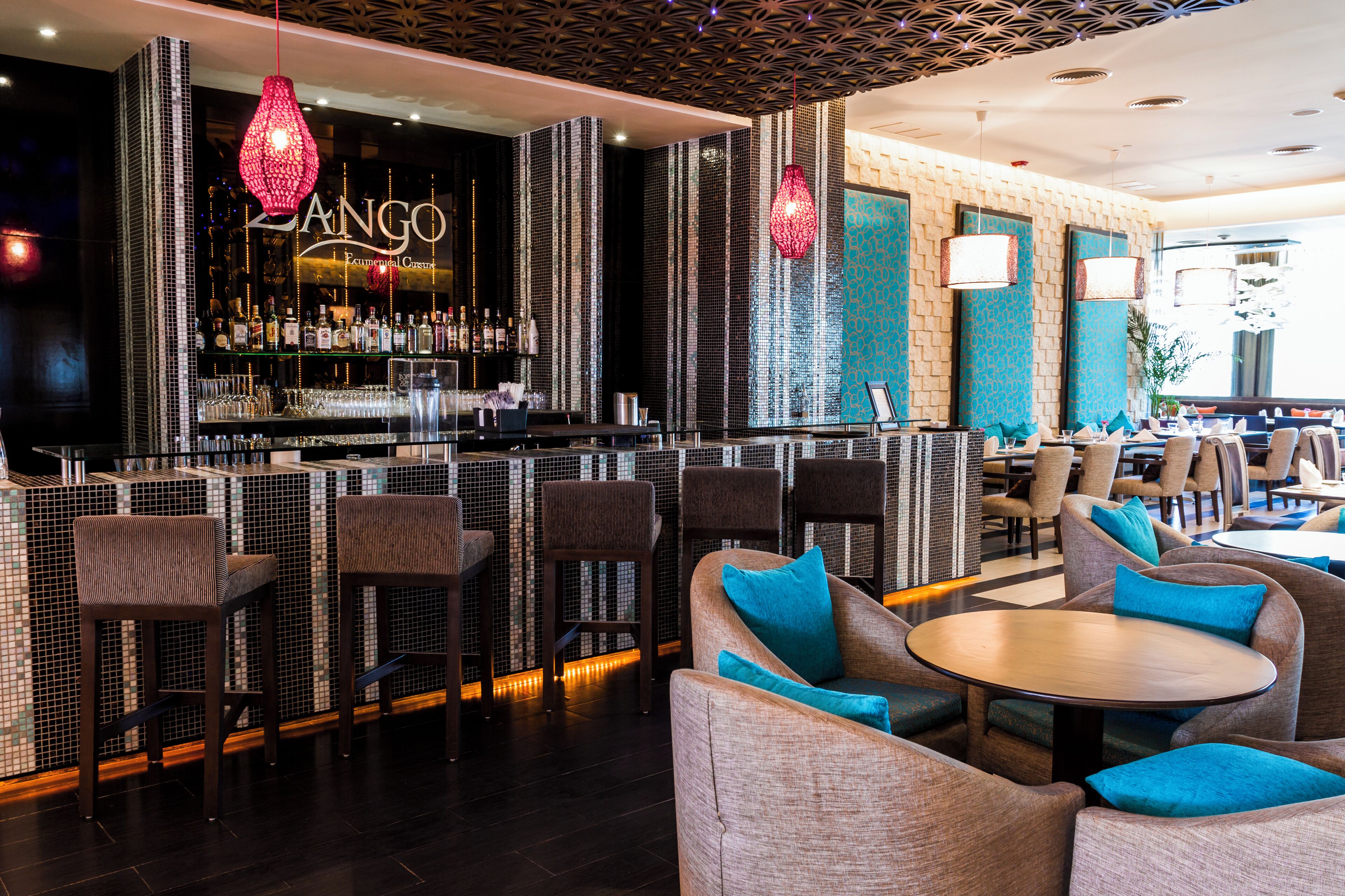 A bar area with a high bar counter, multiple seating options including bar stools and cushioned chairs, and a patterned wall design.