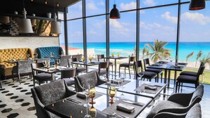 A restaurant with tables and chairs, large windows, and a view of the ocean.